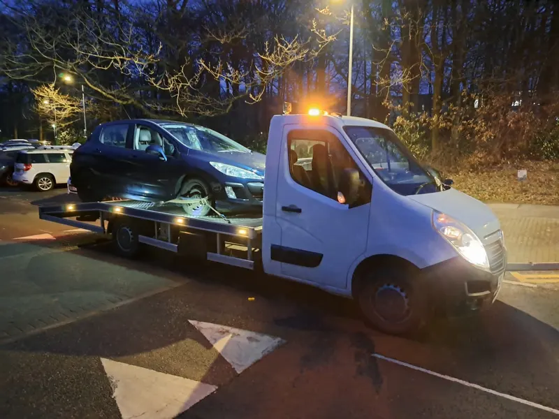 Car on a recovery truck at night, bought for scrap in Bolton